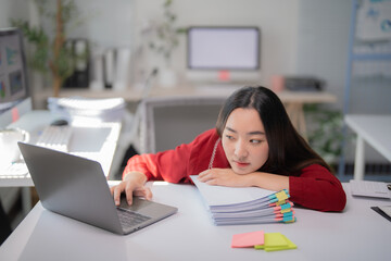 Young asian office worker is feeling bored and tired while working with laptop and staring away,...