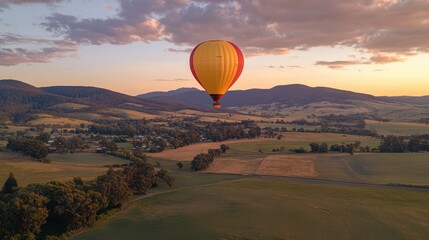 Obraz premium Colorful Hot Air Balloon Soaring Over Serene Landscape During Sunset with Rolling Hills and Lush Greenery in the Background