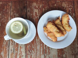 A plate of golden brown banana fritters sits beside a cup of hot lemon.