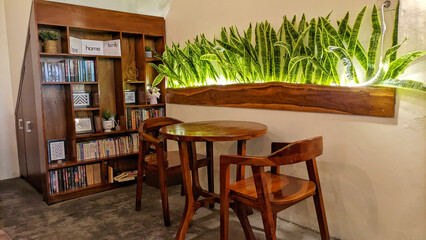 Selective focus of Cafe or restaurant interior design. Empty wooden tables and chairs decorated with green plants with flashing lights and reading books neatly arranged on wooden cabinets.
