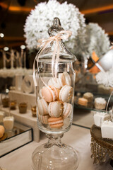 glass vase with lid, decorated with light ribbon. Inside the vase are pastel colored pasta, mostly white and light pink.