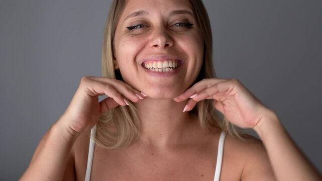 Young caucasian smiling blonde woman showing dimples on her cheek with her hands on a dark grey background. The girl with beautiful smile
