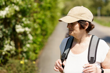 Portrait of a senior woman with a cap and backpack on a country road