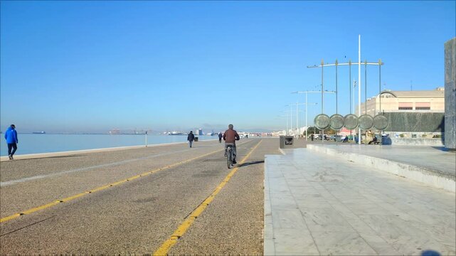 Video of people strolling along the seaside promenade in Nea Paralia, Thessaloniki, Greece, on a crisp winter morning.