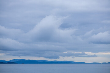 Cloudy Sky Over Calm Sea and Distant Hills in Serene Landscape