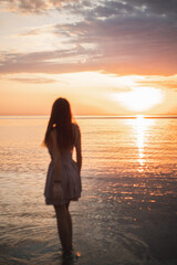 Fototapeta premium Girl at sunrise on the sea. Silhouette of a slender young girl against the backdrop of the rising sun. Summer, sea, rocks. Vacation at sea. Vacation in warm regions.