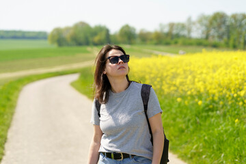 Young woman with a backpack on a country road in a rape field