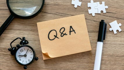 Q&A Concept with Magnifying Glass, Alarm Clock, Puzzle Pieces, and Pen on Wooden Background