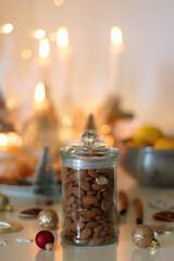 Various Christmas decorations, cookies, chocolate, nuts and tangerines, wine glasses and lit candles on the table. Holiday hygge at home. Selective focus.