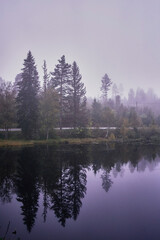 a Norwegian lake surrounded by trees on a dark rainy day