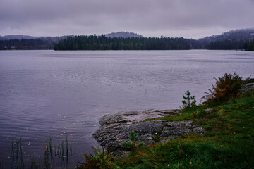 a Norwegian lake surrounded by trees on a dark rainy day