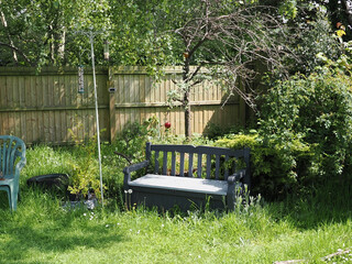 A naturalistic garden with mixed length grass birdfeeder on a pole and a grey plastic bench