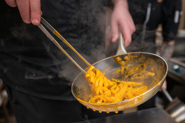A chef expertly tossing fettuccine pasta in a steaming pan. The dish, vibrant in color, is prepared...