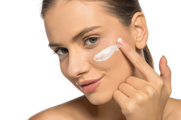 Beautiful young smiling woman applies a face cream on a white studio background.