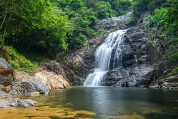 Fototapeta premium Waterfall cascading down lush green forest surrounded by tropical vegetation