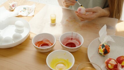 A Woman Paints Easter Eggs at a Sunlit Table, Surrounded by Bowls of Dye and White Eggs.