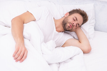 Young man sleeping or napping at home in bed at white bedroom