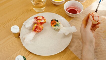 A Plate with Colorful, Wrapped Easter Eggs and a Woman Painting Another Egg.