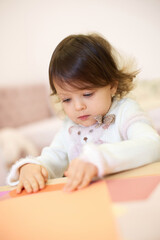 little child girl holding multi-color paper while sitting by table at home