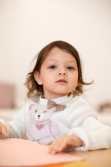 little child girl holding multi-color paper while sitting by table at home