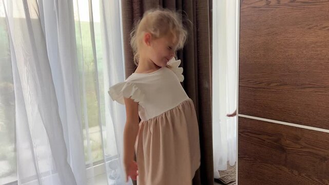 Little girl in dress preening in front of the mirror in home bedroom