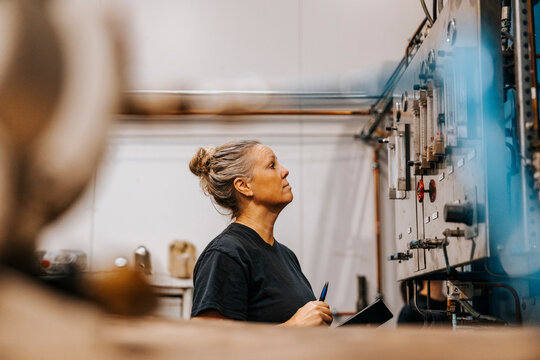 Side view of mature female worker examining circuit in metal factory