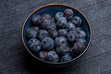 , Deutschland, 18.12.2024,  Nahaufnahme von frischen Blaubeeren in einer blauen Keramikschale auf dunklem Hintergrund. Gesundes Obst, ideal für Ernährung und Wohlbefinden.