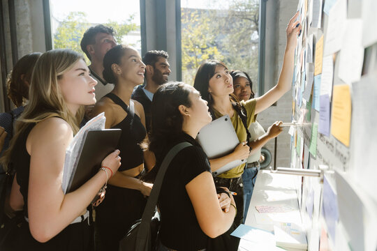 Young woman pointing and reading bulletin board with multiracial students in college