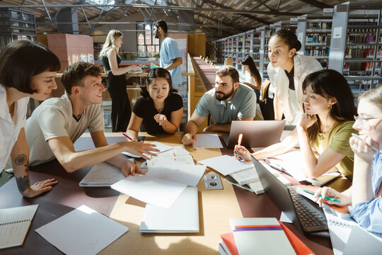 Multiracial male and female students discussing while doing group assignment in library at college