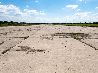 A desolate and abandoned airstrip displaying weathered concrete and overgrown vegetation beneath a bright blue sky