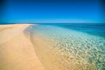 Fototapeta premium Clean sandy beach with no footprints, crystal-clear water meeting the shore, concept of unspoiled natural beauty, bright sunlight, high-definition beach photography