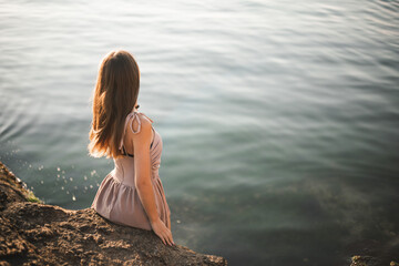 Girl at sunrise on the sea. Silhouette of a slender young girl against the backdrop of the rising sun. Summer, sea, rocks. Vacation at sea. Vacation in warm regions.