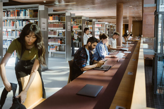Multiracial male and female sitting in row while studying at university library
