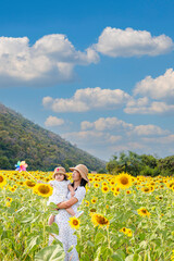 Fototapeta premium Mother carries daughter in sunflower field,Carefree mother and daughter spending leisure time in sunflower field