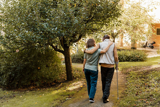 Rear view of female nurse walking with arm around elderly male at park