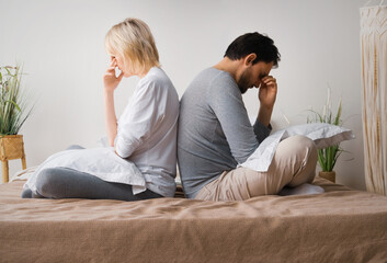 Unhappy sad couple, brunette man, blond woman, husband and wife sit on home bed, turned away back...