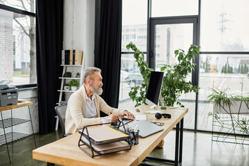 Senior man engages in work at a sleek desk surrounded by greenery and natural light.