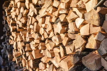 Selbstklebende Fototapeten Stacked firewood logs illuminated by sunlight, creating a rustic winter texture © Наталья Самойлова