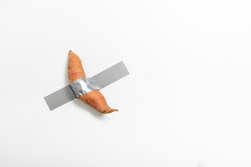 A sweet potato is secured to a wall using duct tape, showcasing a unique approach to conceptual art. This artwork combines everyday objects with an unconventional presentation.