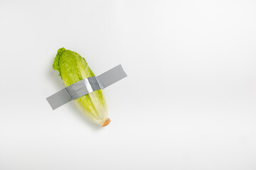 A head of lettuce is firmly attached to a wall with gray duct tape, creating an unusual visual...