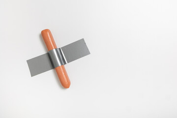 A sausage is firmly fixed to a white wall using duct tape, presenting a unique concept in modern...