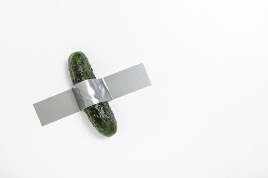 A cucumber is affixed to a wall using duct tape, illustrating a unique blend of food and conceptual art. This creative display prompts thoughts on everyday objects and artistic expression.