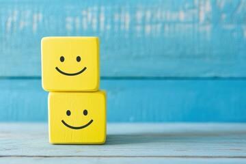 Two cheerful yellow blocks with smiley faces stacked on a rustic wood table, conveying happiness and positivity against a blue background for a vibrant stock photo setting