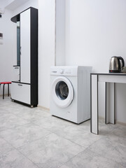 The washing machine stands in the hallway against the background of light furniture. Interior of a small budget apartment.