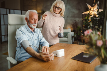 senior wife support and help her senior husband to measure blood pressure