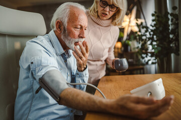 senior woman help her senior husband to measure blood pressure at home