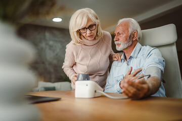 senior woman help her senior husband to measure blood pressure at home