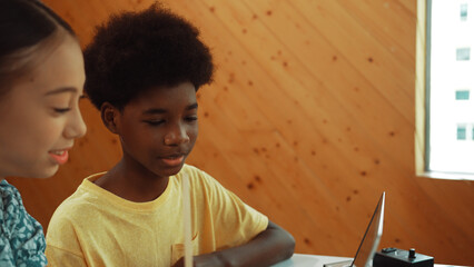 Site view of african boy and caucasian girl in casual cloth working together to coding prompt or programing system at table with laptop and electronic equipment at STEM technology class. Edification.