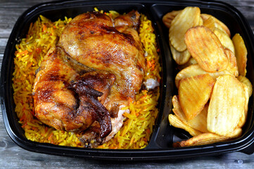 Arabic Syrian cuisine of machine grilled barbecued chicken with colorful Basmati rice and fried thin chips potatoes served in a black disposable plate, usually served with garlic sauce and pickles