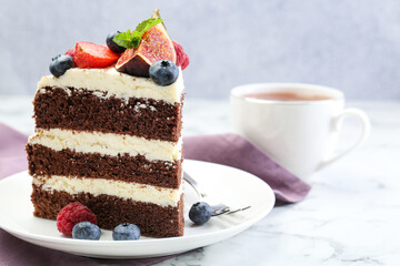 Piece of delicious chocolate sponge cake with berries and tea on white table, closeup